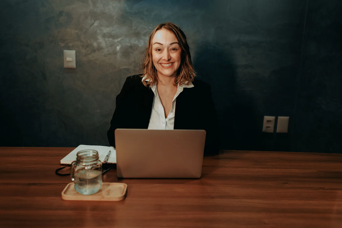 Consultora sorrindo à mesa do escritório, com notebook e caderno, pronta para atender
