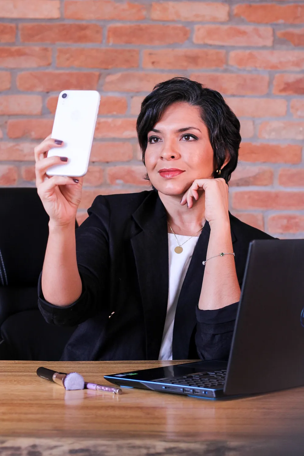 Mulher sorrindo enquanto olha o celular, sentada à mesa de trabalho