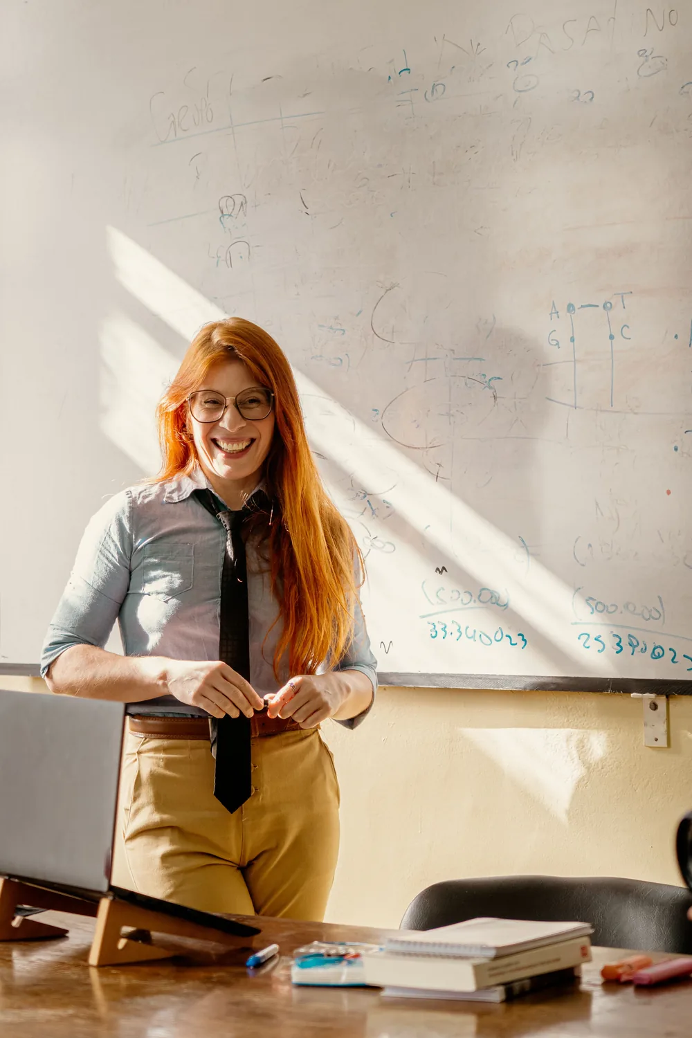 Professora sorrindo em frente ao quadro branco da sala de aula
