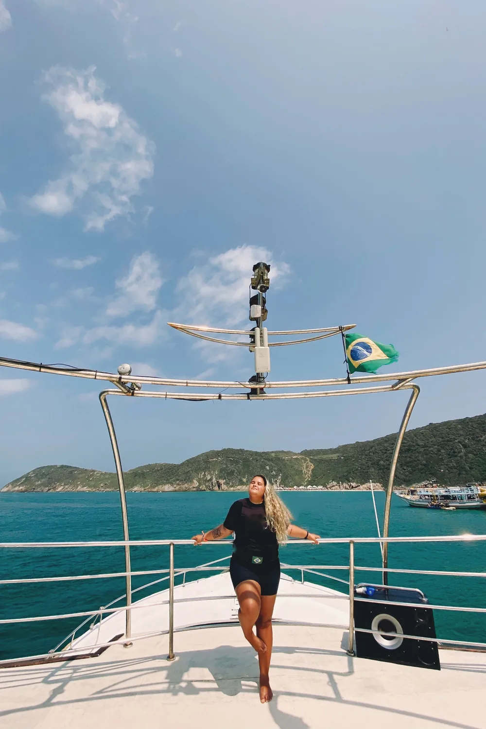 Mulher aproveitando o sol na proa de um barco, no mar azul de Arraial do Cabo